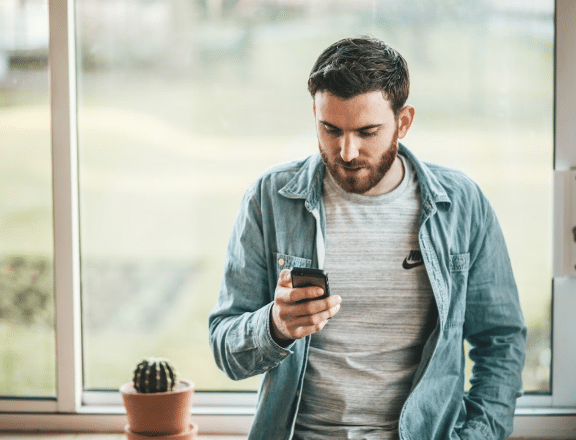 a photo of a man looking at his phone standing next to a small potted cactus